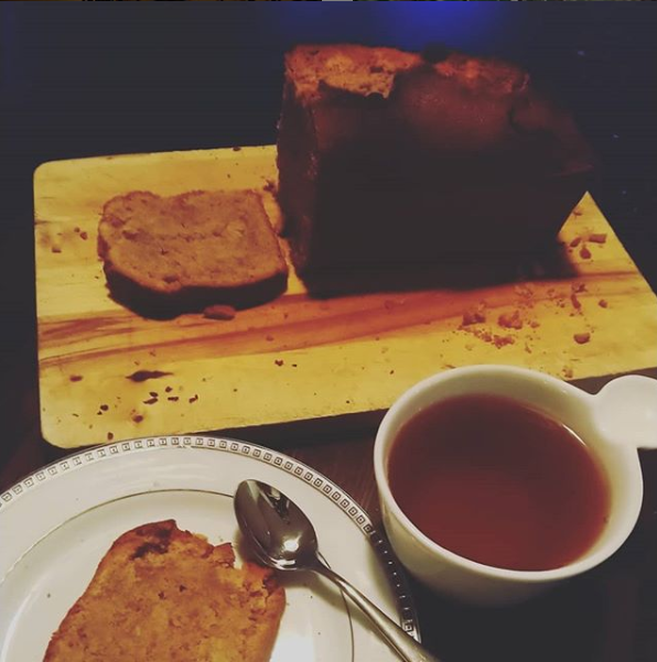 Un gâteau appelé Brun kage avec une tranche coupée sur une planche en bois. A coté d'une tasse de thé et d'une assiette avec une part de gâteau dedans.